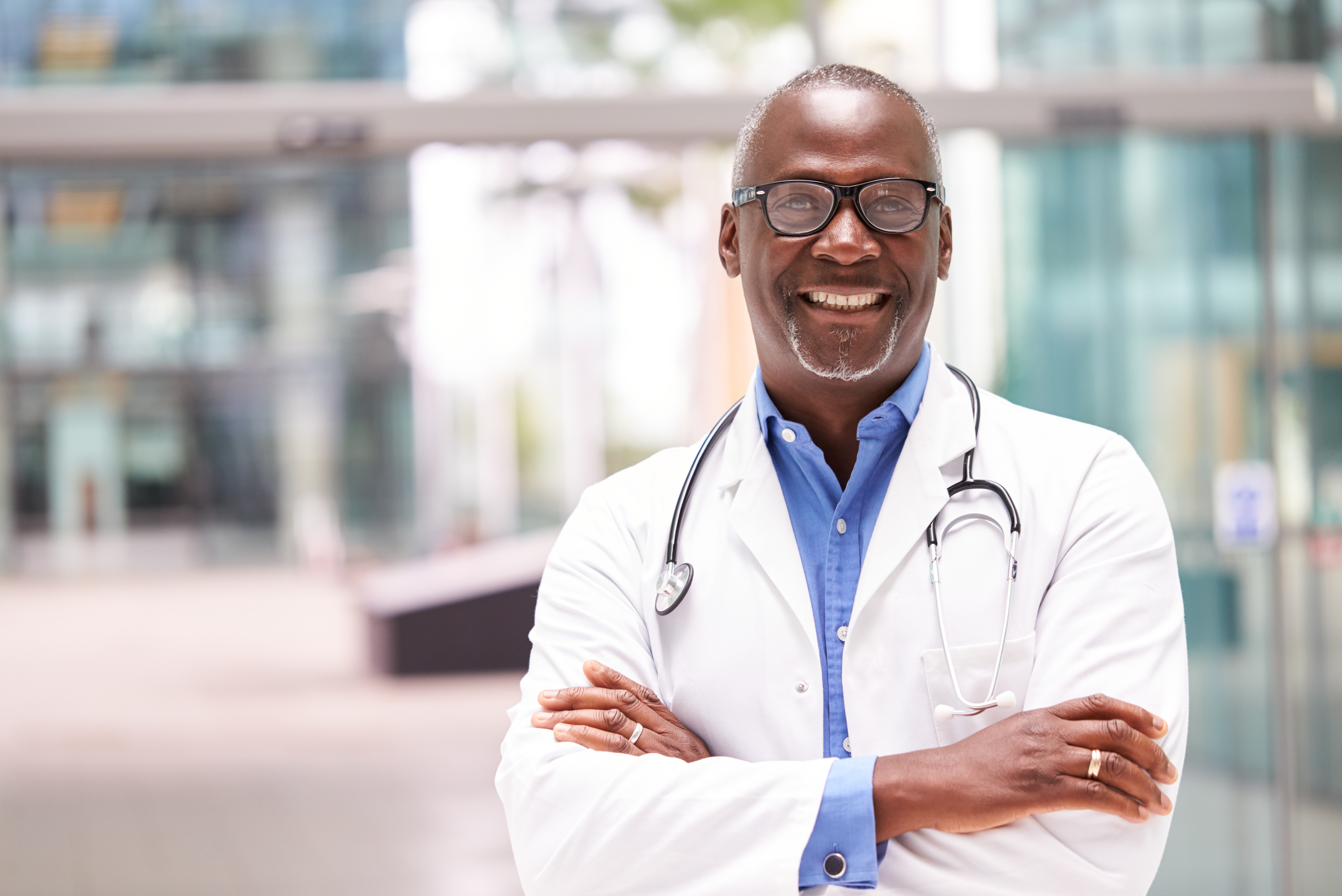 Portrait Of Male Doctor With Stethoscope Wearing White Coat Standing In Modern Hospital Building